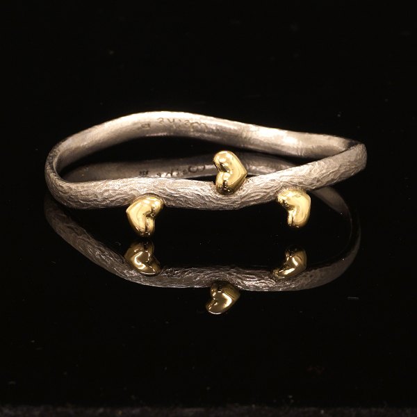 Michale Weihe: Oval armring i sterlingsølv med tre hjerter udført i 18kt guld. 
Indv. mål: 5,5x6,4cm. B: 0,6cm. V: 32gr