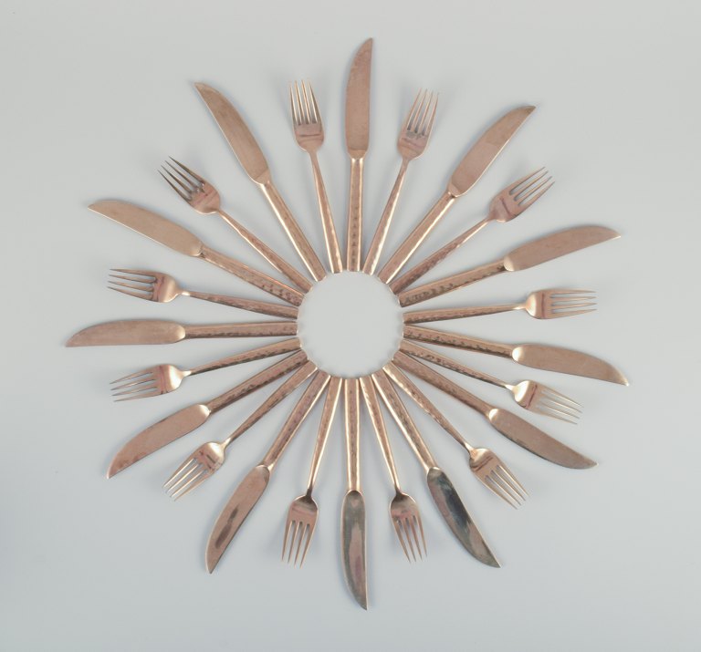 Scandinavian designer. Twelve-person dinner service consisting of twelve dinner knives and twelve dinner forks in handcrafted hammered brass. High-quality craftsmanship.